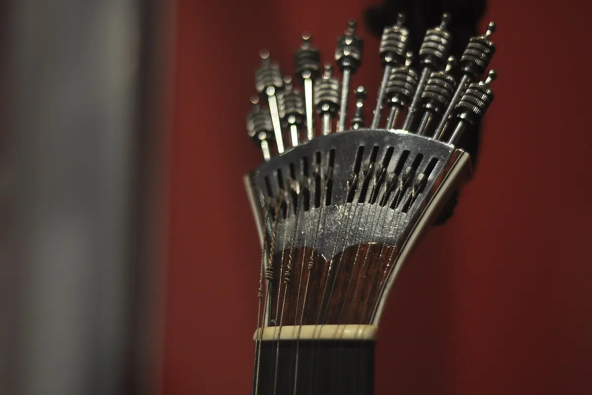 The fan-shaped tuning mechanism of a Portuguese guitar against a red wall, with a row of tuning pegs fanning out from the head