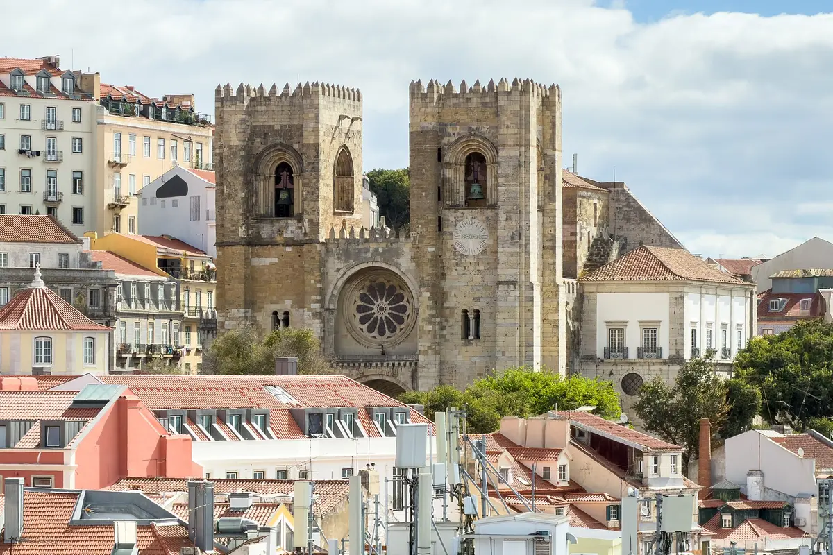Lisbon Cathedral, a pale stone church with two crenellated towers and a round rose window, seen over terracotta rooftops